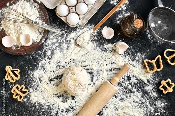 Fototapeta Cooking dough for cookies, butter, eggs, cooking equipment, flour on a black table. Top view with copy space, mockup for menu, recipe or culinary classes. Baking background.