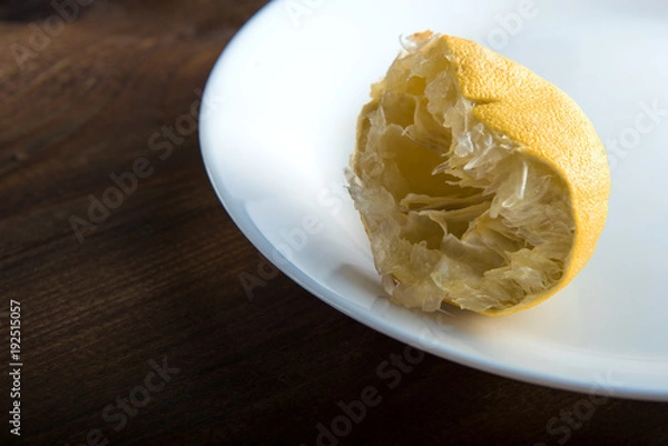 Fototapeta the squeezed-out lemon on a white plate on a wooden background