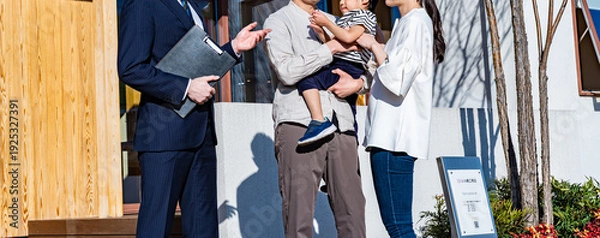 Obraz スーツの営業マンが家族（夫婦と子供）に新築住宅を案内しているシーン