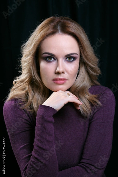 Obraz Portrait of beautiful model with curly light hair on black background. A hand rested to her chin.
