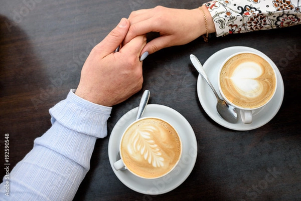 Obraz Coffee cups and holding hands at the darken wooden table