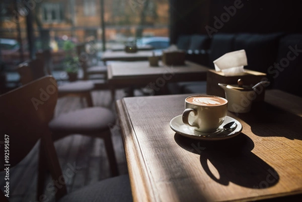 Obraz A cup of coffee on the wood table and sunlight with cozy cafe interior background
