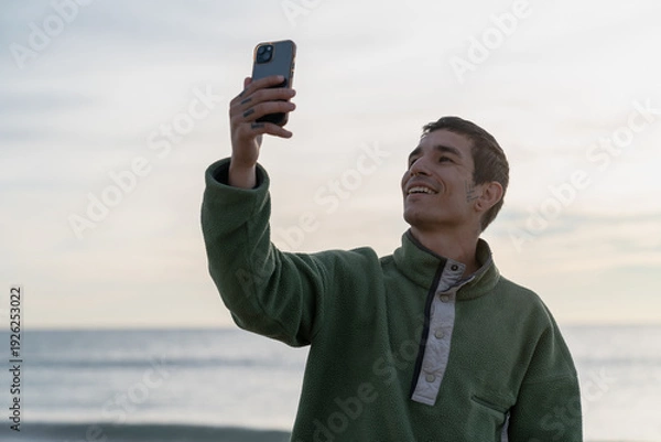 Obraz Young man smiling taking selfie by ocean