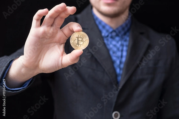 Fototapeta young businessman holds a gold coin bitcoin