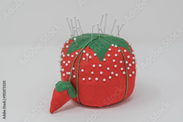 Fototapeta Studio shot of an isolated red pin cushion in the shape of a strawberry, stuck with white glass pins