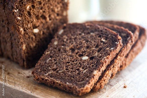 Fototapeta Whole-wheat bread with seeds cut on a wooden board on a natural background. Healthy food, healthy food.
