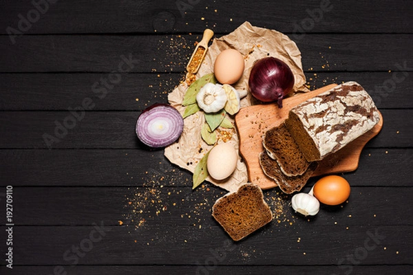 Fototapeta Bread, eggs, garlic, onions, seasonings and various spices lie on a dark background.