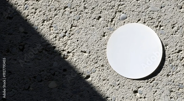 Obraz A white circular object casting a shadow on a textured concrete surface.