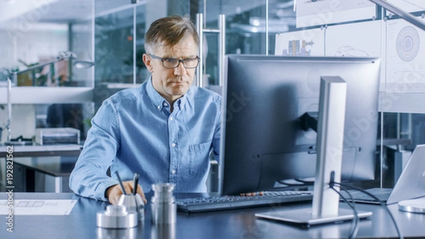 Fototapeta Doświadczony inżynier przemysłowy pracujący na komputerze osobistym w stylowym, nowoczesnym, przeszklonym biurze.