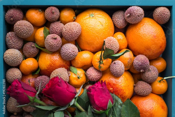 Fototapeta Gift set for the girl. A box of fresh fruit with red oranges, mini tangerines, lychee fruits and red roses