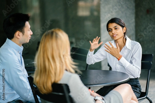Fototapeta A portrait of an intelligent and young Indian Asian woman being interview  for a job. She is dressed professionally in a white shirt and is sitting and talking to her interviewers.