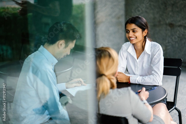 Fototapeta A young and attractive Indian Asian woman is interviewing for a job. She is dressed professionally in a white shirt and is sitting and talking to her interviewers. She is confident and relaxed