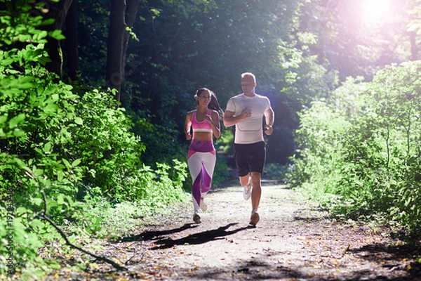 Obraz Athletic man and woman doing Jogging in the forest with sun rays.