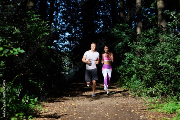 Obraz A man and a woman sporting on a Sunny day, jog along the forest path.