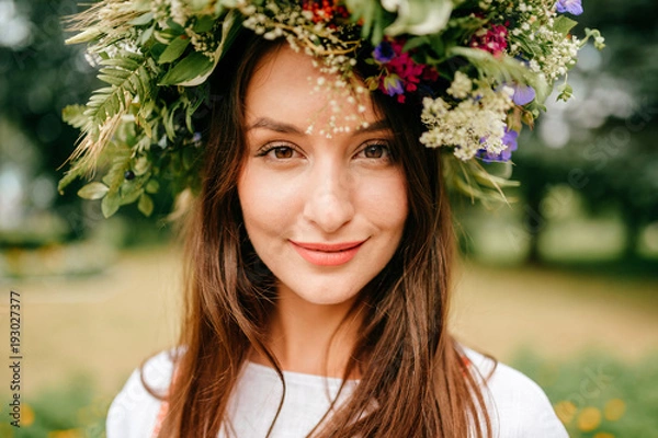 Obraz Closeup portrait of beautiful young girl in traditional Slavic dress with wreath of summer flowers. Ethno folk style cheerful female on abstract background in summer at floral feast. Expressive face.