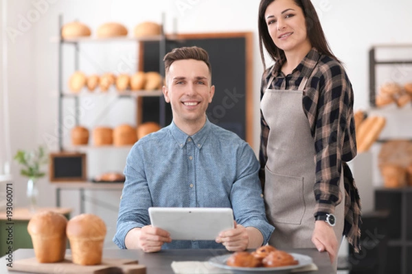 Obraz Young people using tablet computer in bakery. Small business owners