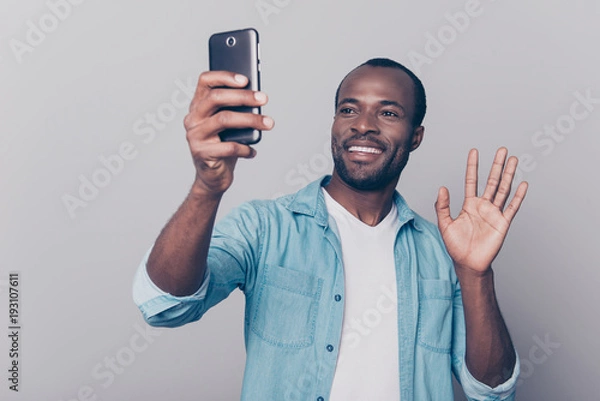 Fototapeta Portrait of cheerful, positive, professional man making selfie on his gadget, electronic, device, holding smart phone in hand, having video-call, sending hello to friend, isolated on grey background