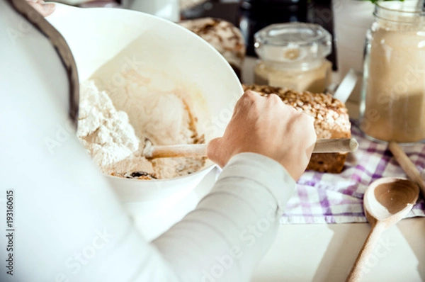 Fototapeta Close-up on the hand of a woman preparing a dough for homemade bread. Photo taken in the light of natural sun and studio lamps. It contains delicate artistic noise and a vintage color grading