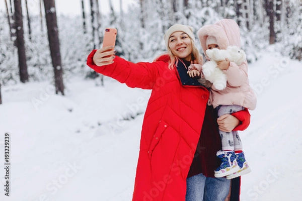 Fototapeta the mom holds a small daughter doing a selfie in the snowy picturesque area of the pine forest on the highway
