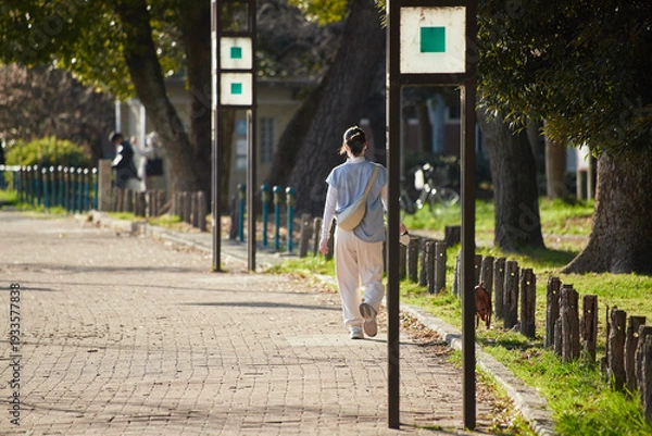 Obraz 春の名城公園で犬を連れて散歩する若い女性の姿