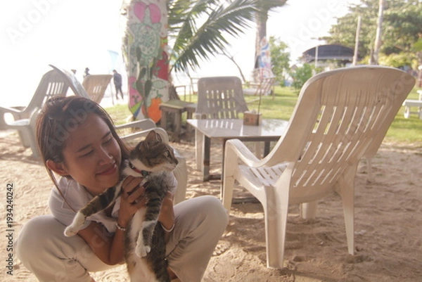 Obraz 태국 해변 카페에서 고양이와 함께 여유로운 휴식을 즐기는 아름다운 태국 여성의 이국적인 라이프스타일
