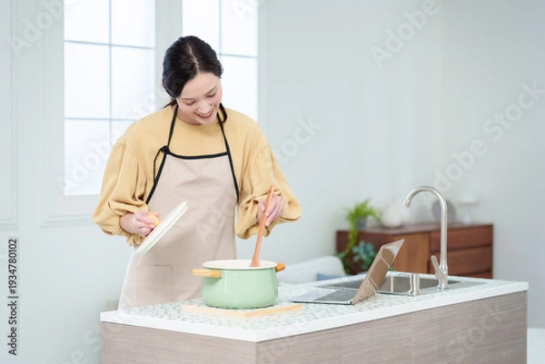 Obraz キッチンでパソコンを見ながら料理をする主婦