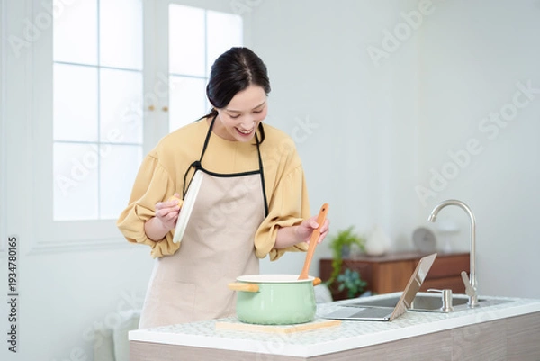 Obraz キッチンでパソコンを見ながら料理をする主婦