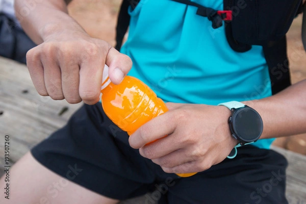 Fototapeta Bottle of orange juice in hands of trail runner visitor