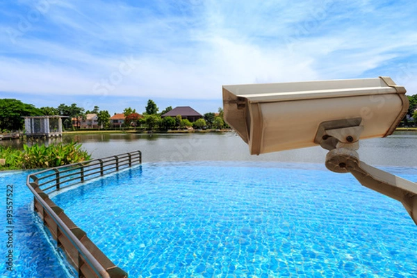 Fototapeta CCTV security camera secure to protect and outdoor swimming pool and lake with beautiful sky. Copy space.