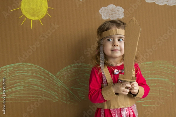 Obraz Portrait of a playful baby with a cardboard sword and a suit. handmade. background of painted sun and white clouds