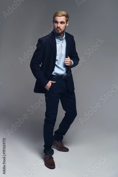 Fototapeta Stylish and professional. Fashionable entrepreneur holding lapel and put the other hand into the pocket in front of grey background.