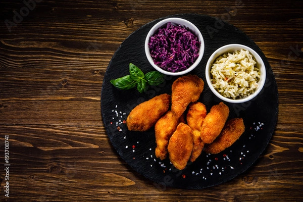 Fototapeta Fried chicken nuggets with cabbage served on black stone on wooden table