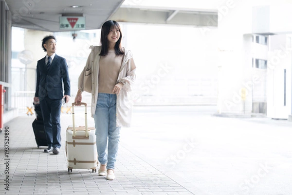 Obraz 空港や交通機関のターミナルで出発するスーツケースやキャリーケースを持つ歩く女性　旅行や休日、トランジットのイメージの全身