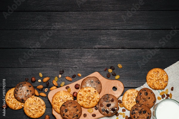 Fototapeta Freshly baked cookies on a wooden table. On the table is a board, a glass of milk, around various nuts, almonds and raisins.