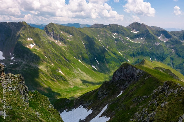 Fototapeta valley with snow in summer mountains. gorgeous mountainous landscape of Carpathians. rocky cliffs and grassy hillsides under a cloudy sky. Fagaras ridge of Southern Carpathian mountains, Romania