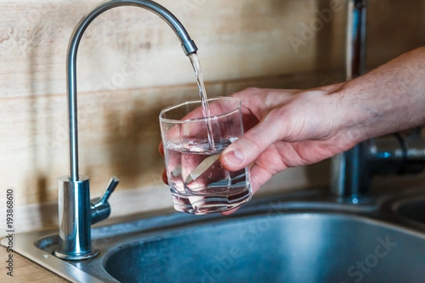 Obraz hand holding a glass of water. a man  pouring water from filter tap. clean water and healthy life concept