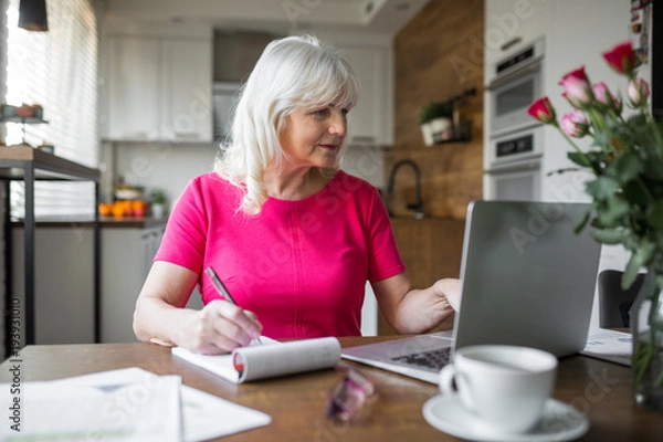 Fototapeta Senior lady working at kitchen table using notebook