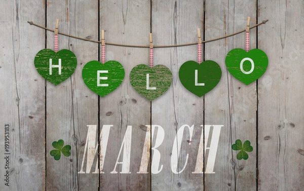 Fototapeta Hello March written on hanging green hearts and weathered wooden background, with clover