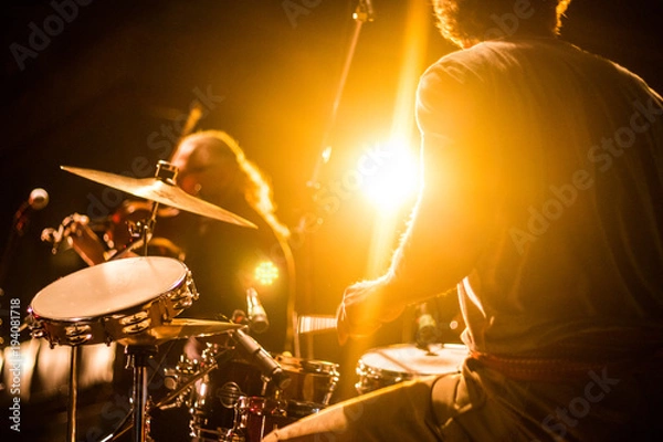 Fototapeta Drummer on stage playing with a band with gold yellow light shining in background 