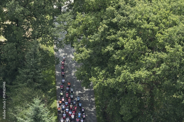 Fototapeta aerial image of cycling tour de l'Avenir, the peloton crossing a forest