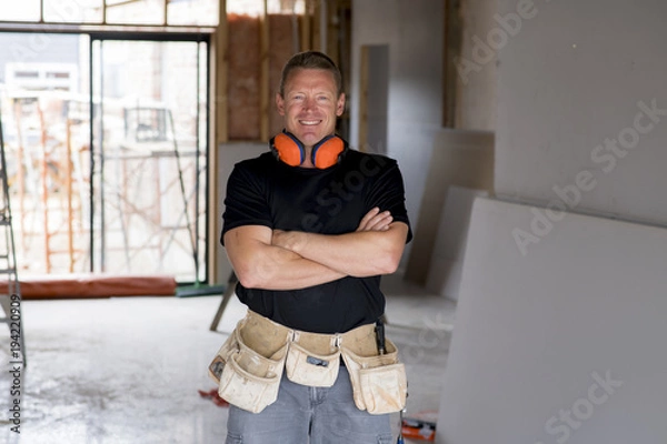 Obraz attractive and confident constructor carpenter or builder man with ear protection gear working happy at industrial construction site