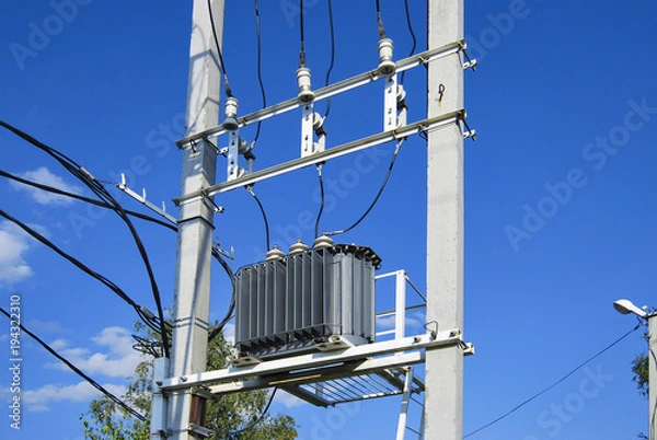 Fototapeta An electrical distribution transformer with cooling fins is located on the pole. Against the blue sky.
