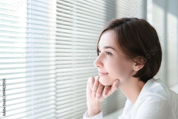 Fototapeta 窓のブラインドから外を見つめる女性