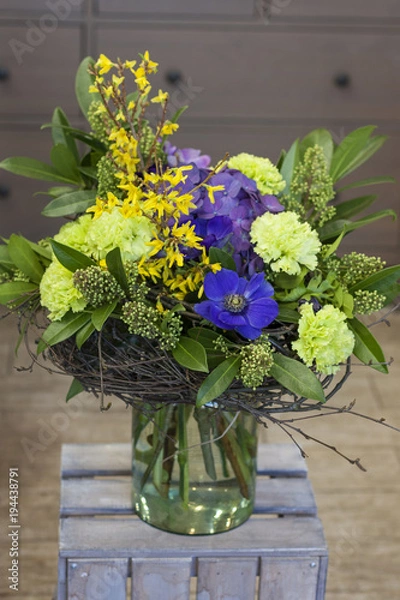 Obraz Оригинальный букет цветов с березовыми ветками стоит в стеклянной вазе на деревянном ящике 