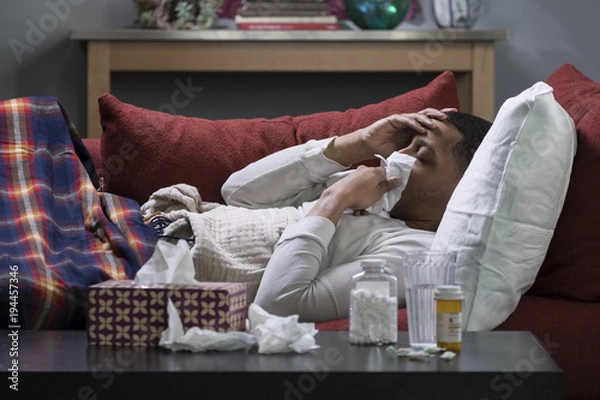 Fototapeta Man laying on a sofa coughing and sneezing