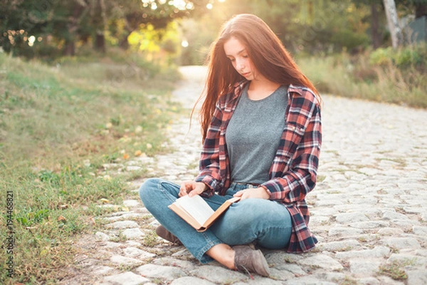 Obraz A young female is sitting on ground and reading book