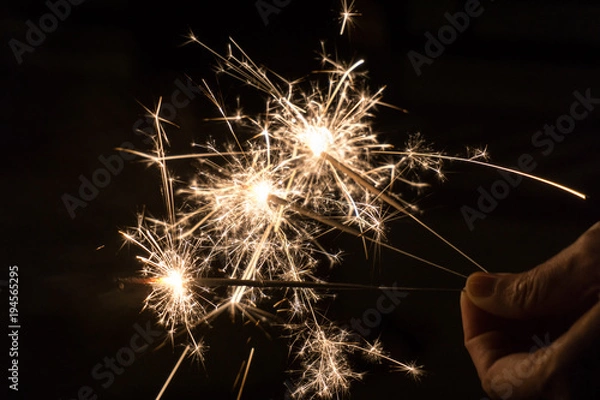 Fototapeta Hand holding golden sparklers shining  in the dark at nigh for birthday party and celebrate new year.
