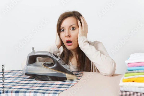 Fototapeta Close up fun tired shocked housewife in light clothes ironing checkered shirt, clothing on ironing board with iron. Woman isolated on white background. Housekeeping concept. Copy space advertisement.
