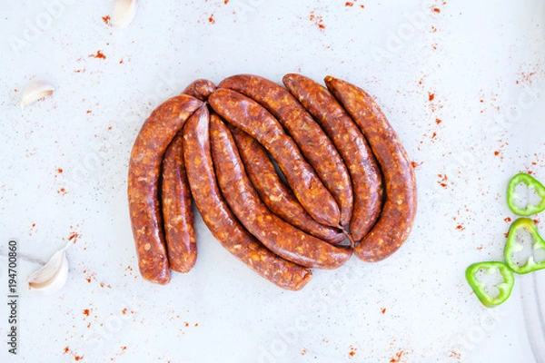 Fototapeta Bundle of raw sausages on a white background with a paprika, top view