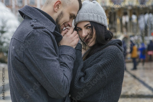 Fototapeta Gorgeous beautiful caucasian woman with a man on a walk in european city at winter. Couple wear casual grey outfit and hugging each other. Cold weather, christmas lights on a background